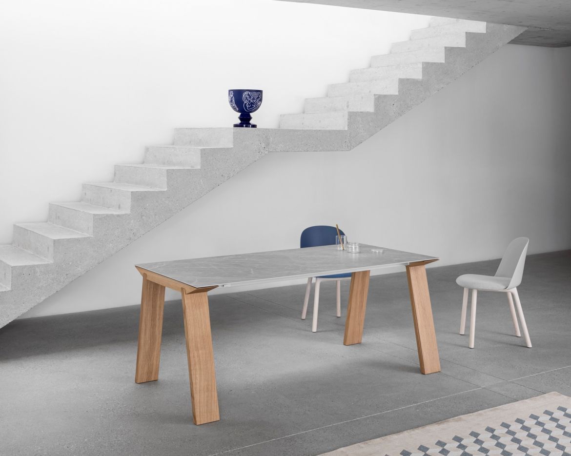 Un tavolo da pranzo moderno con gambe in legno e piano chiaro, vicino a sedie bianche e una scala.