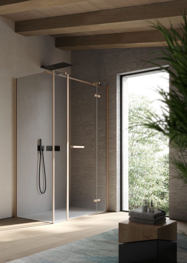 Box doccia moderno con porte in vetro, telaio color bronzo e accessori neri in un bagno luminoso.