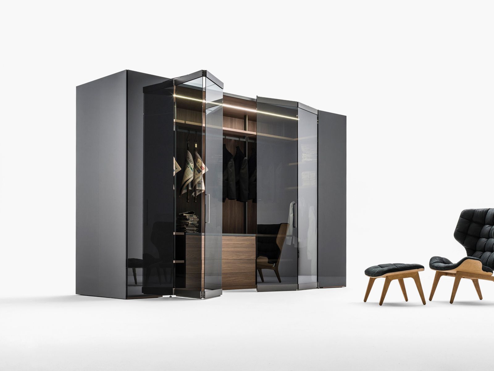 Moderna cabina armadio grigio scuro con ante in vetro, interno illuminato e sedia.