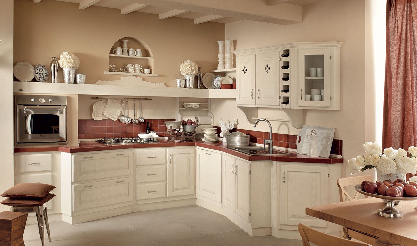 Cucina color crema con mobili curvi, ripiani rossastri e un tavolo da pranzo decorato con fiori.
