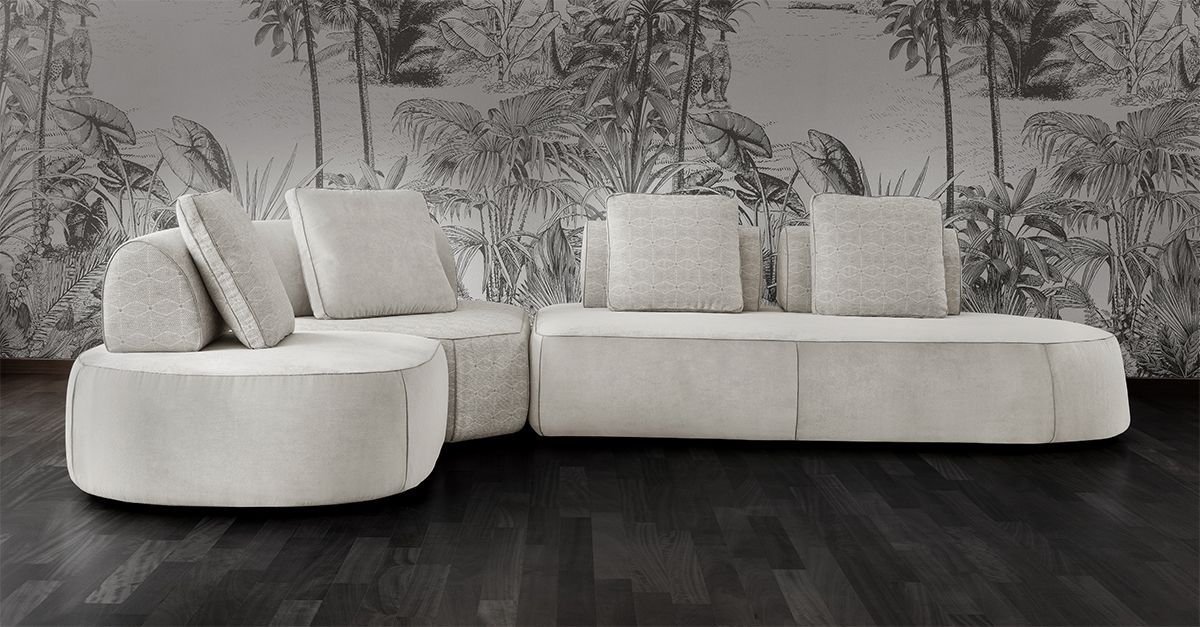 Divano componibile color crema con grandi cuscini su un pavimento in legno scuro e una carta da parati botanica in bianco e nero.