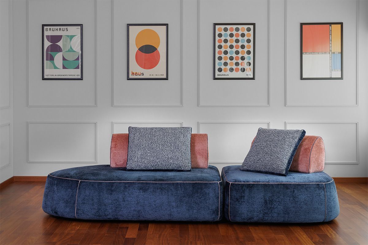 Divano modulare blu con cuscini decorativi contro una parete rivestita di pannelli bianchi con stampe artistiche.