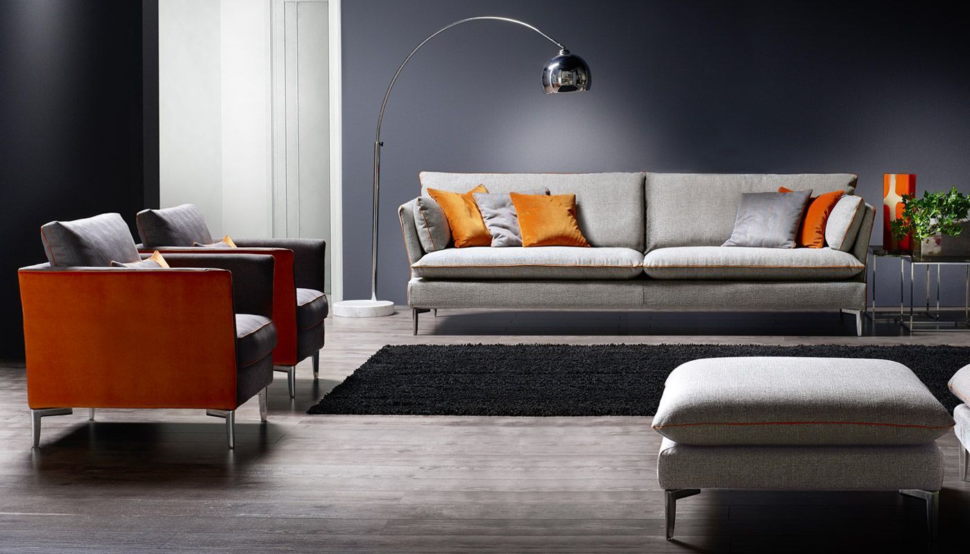 Soggiorno con divano grigio, poltrone arancioni e grigie, tappeto e lampada da terra.