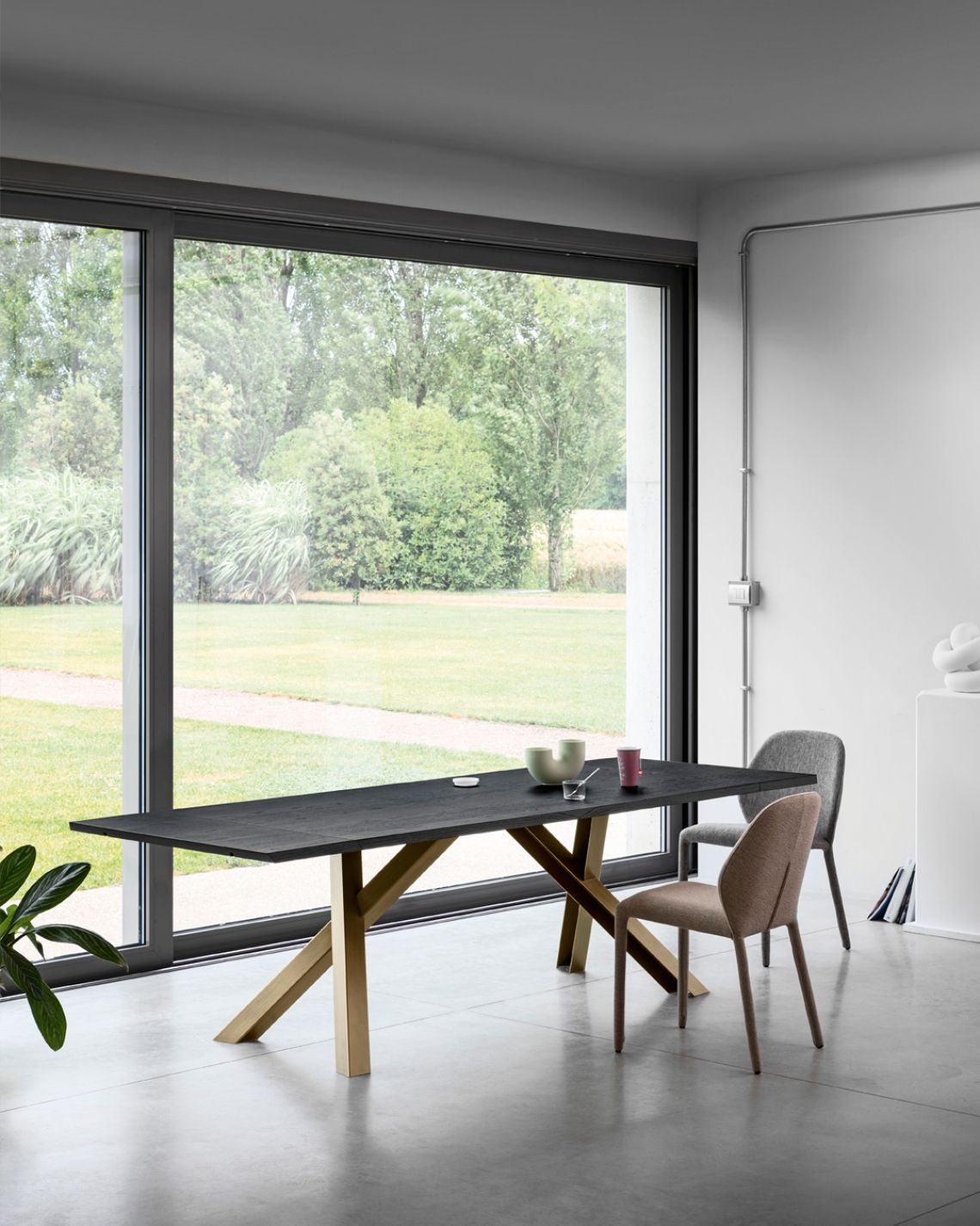Tavolo da pranzo con piano scuro e gambe dorate, due sedie e ampia finestra con vista sull'esterno.
