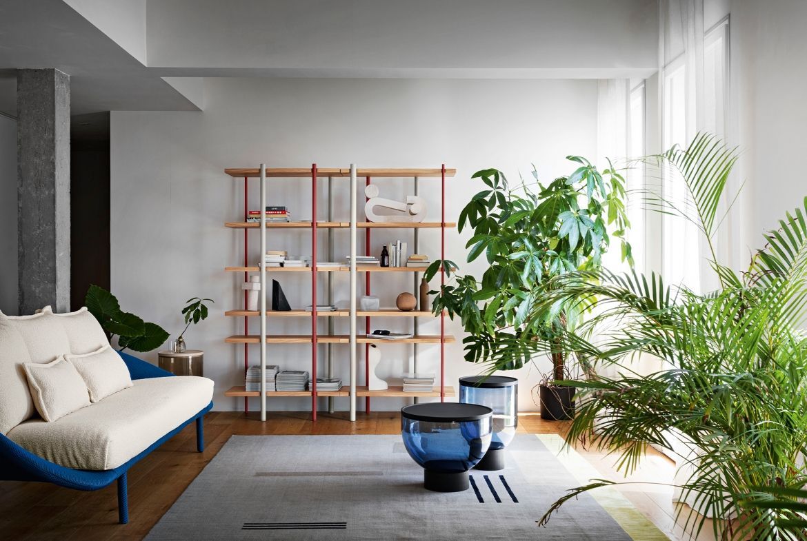 Soggiorno con divano blu, libreria in legno e piante rigogliose.