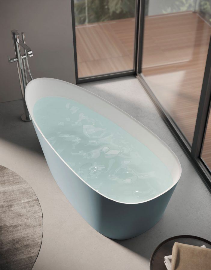 Vasca da bagno ovale blu piena d'acqua accanto a una grande finestra.