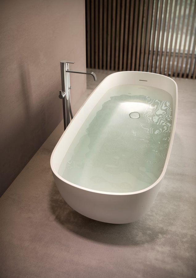 Vasca da bagno bianca piena d'acqua; rubinetto argentato su una superficie di cemento.