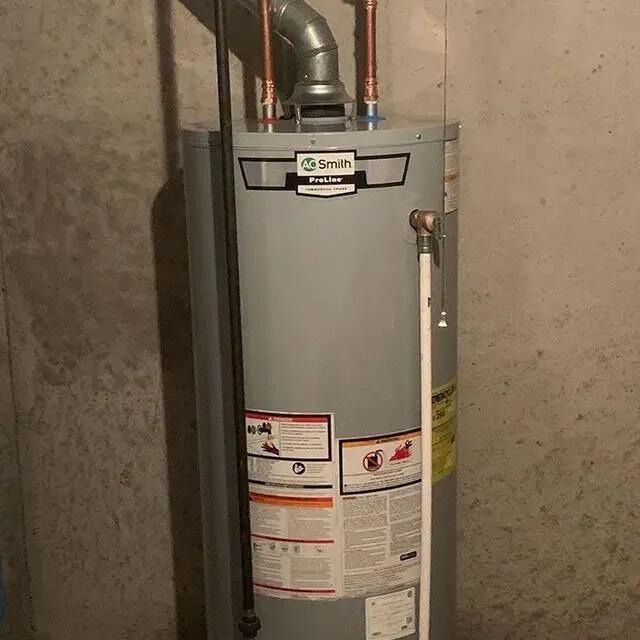 A water heater is sitting in a basement next to a wall.