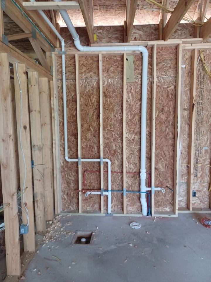A room in a house under construction with pipes coming out of the wall.