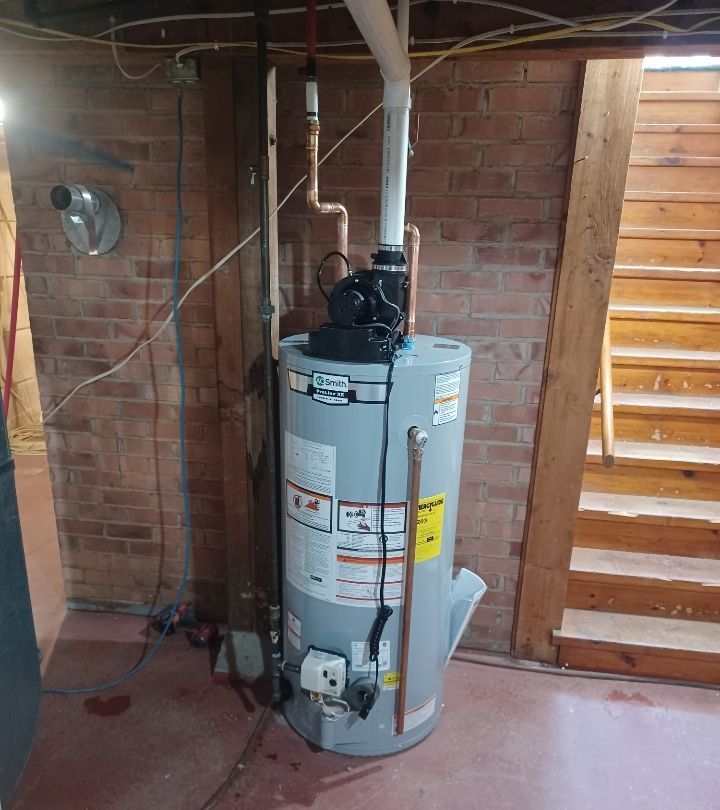 A water heater is sitting in a basement next to a brick wall.