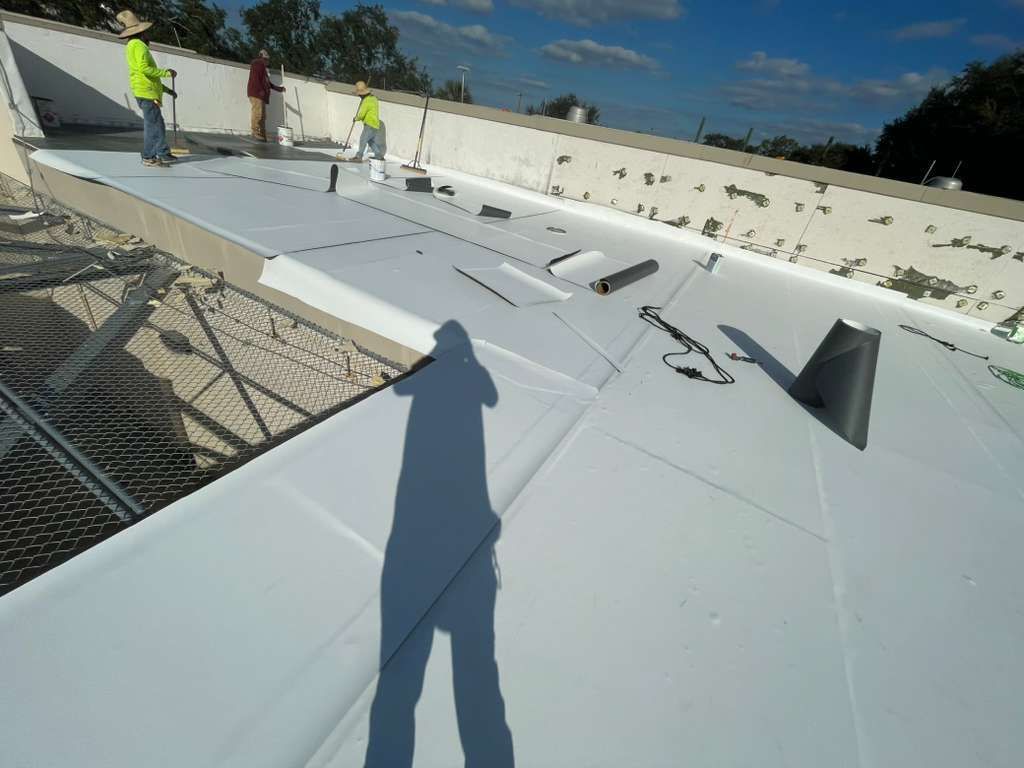 Roofing crew installing TPO flat roof membrane on commercial property in Orlando Florida.