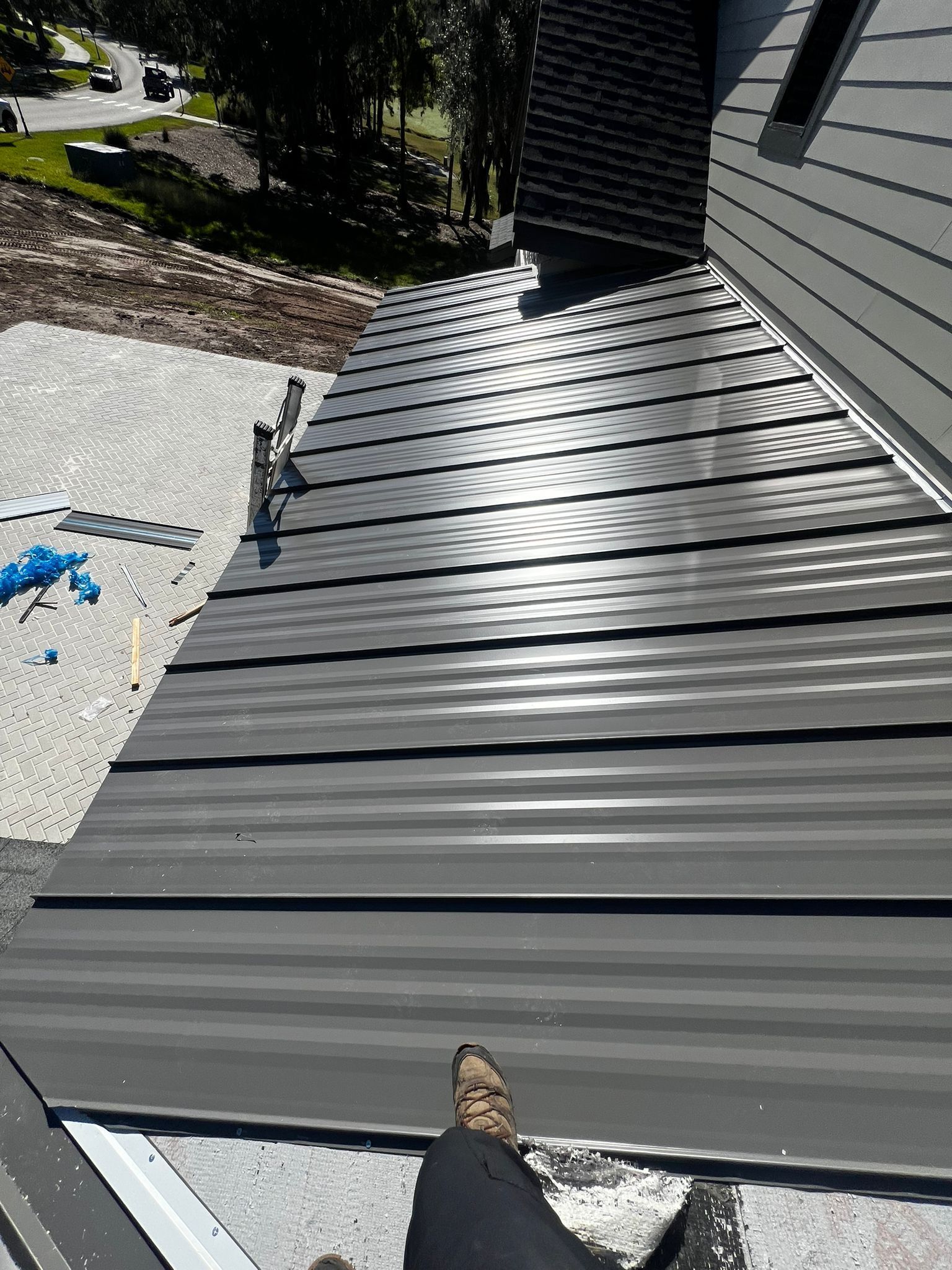 Roofer in Orlando FL installing standing seam metal roof during sunset — highlighting steel tariff impact on metal roofing costs.