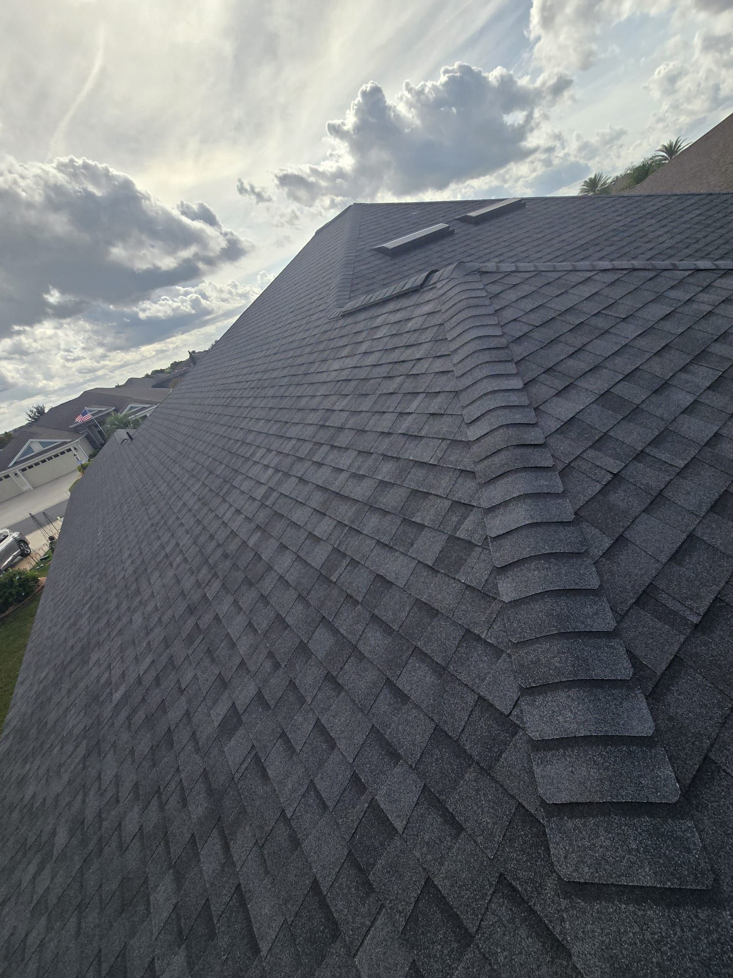 Wide-angle view of a dark shingle roof under a cloudy Florida sky in Polk County, highlighting residential shingle roofing on a sloped roof.