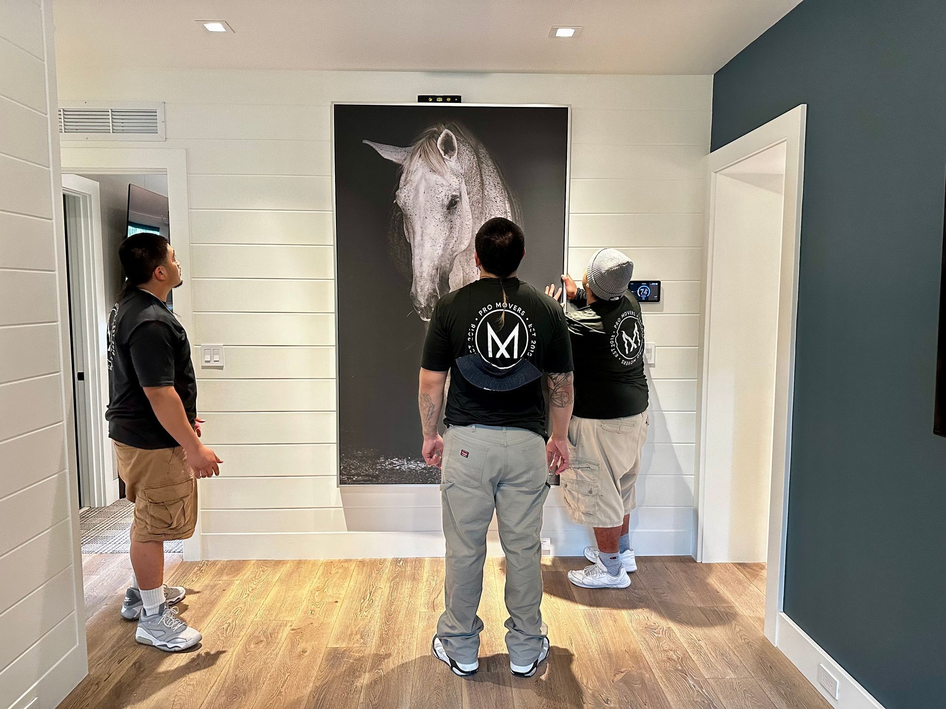 Three men are standing in front of a large painting of a horse.