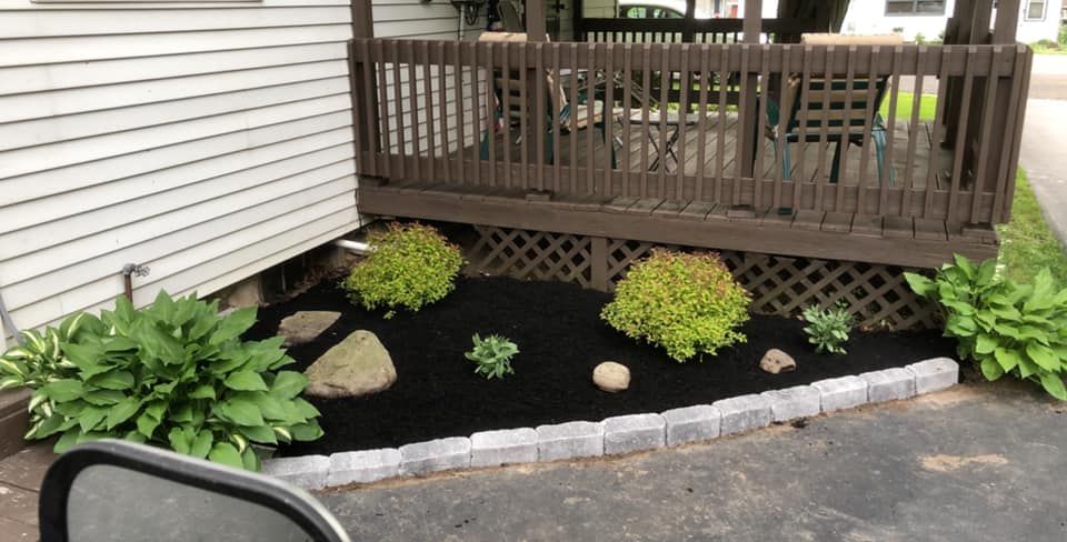 A garden with plants and rocks in front of a house with a porch.