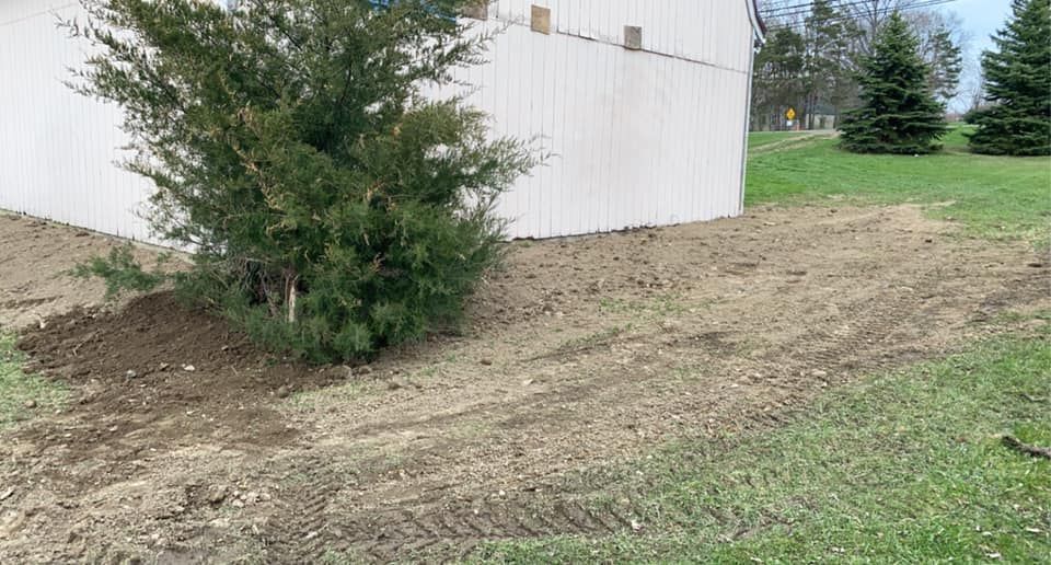 A white building is sitting on top of a dirt hill next to a tree.