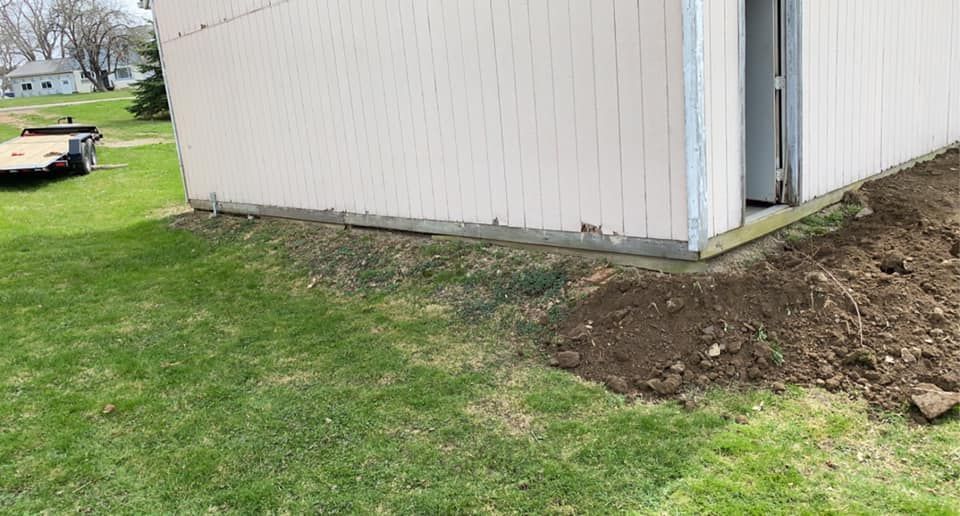 A white shed is sitting on top of a lush green lawn next to a pile of dirt.