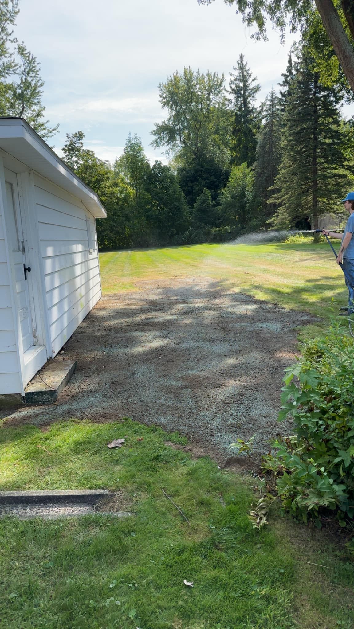 A man is standing in front of a white shed in a yard.