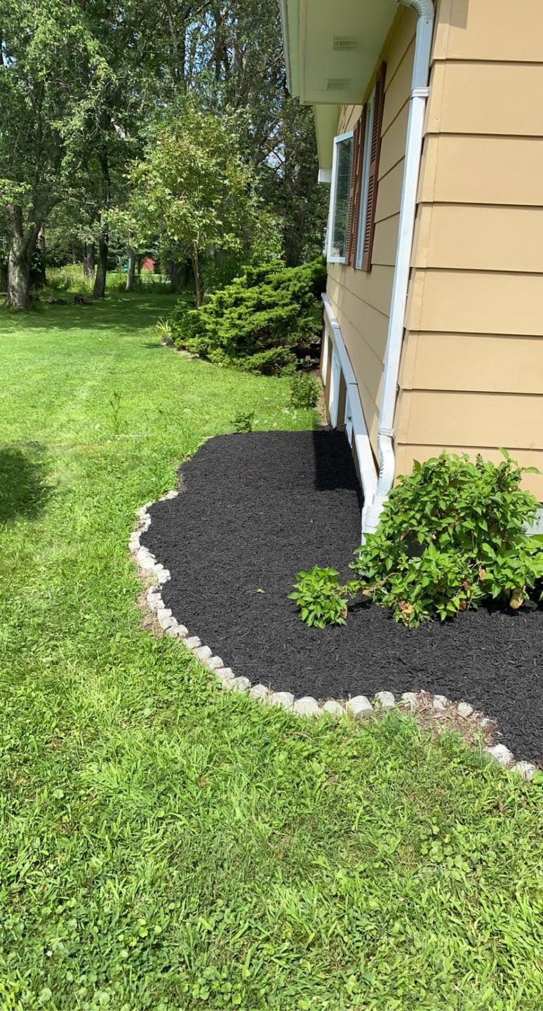 A house with a lush green lawn and black mulch on the side of it.