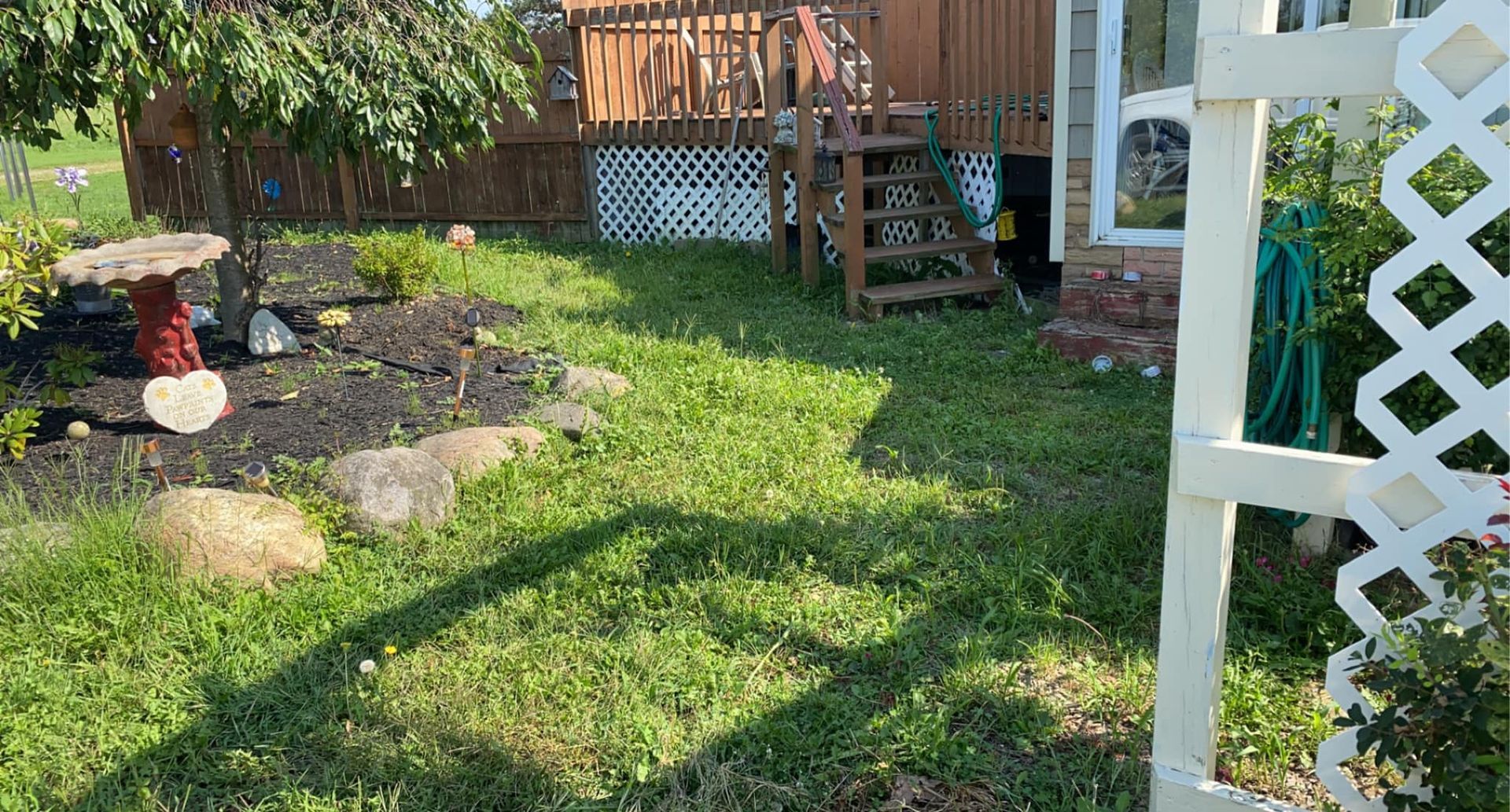 A yard with a white archway leading to a house.