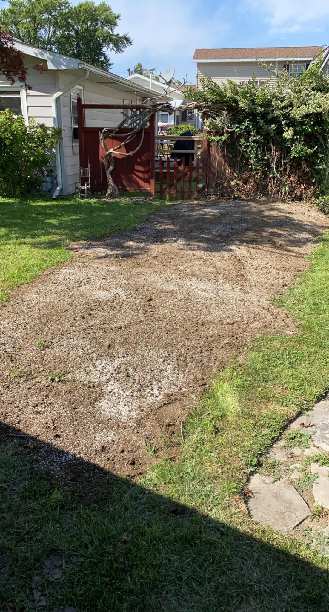 A dirt road leading to a house with a red garage door.