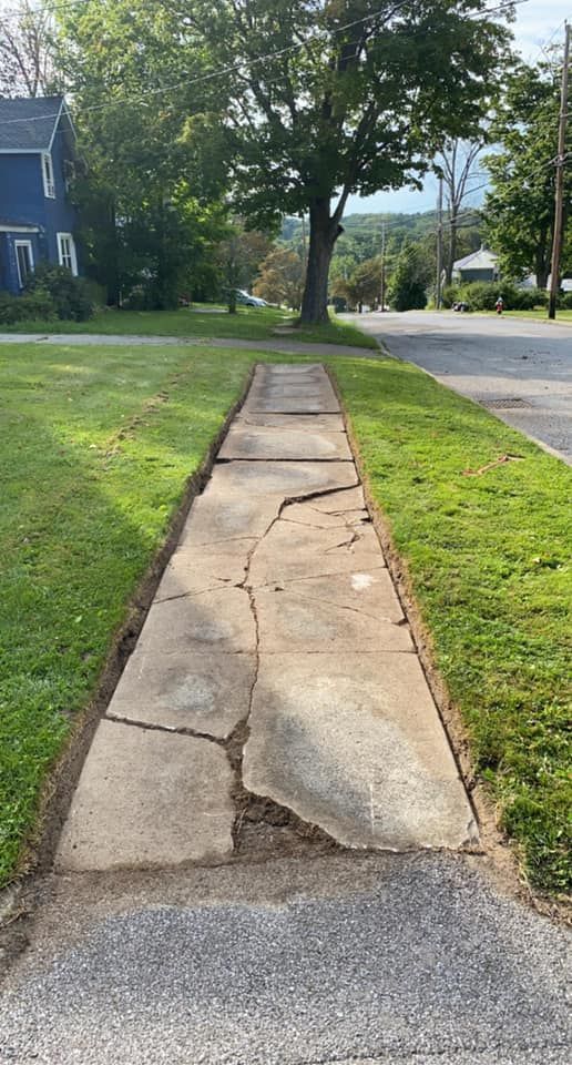 A cracked sidewalk leading to a house on the side of the road.