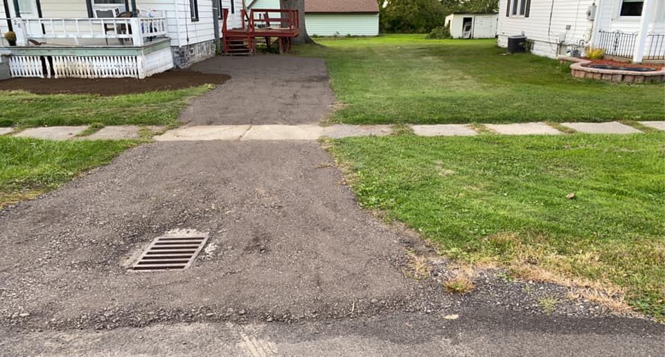 A driveway leading to a house with a drain in the middle of it.