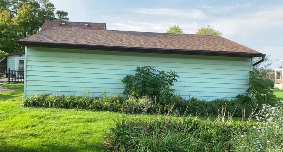 A green house with a brown roof is sitting on top of a lush green field.
