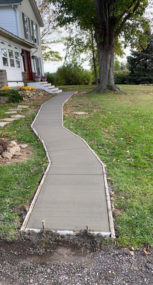 A concrete walkway leading to a house with a tree in the background.