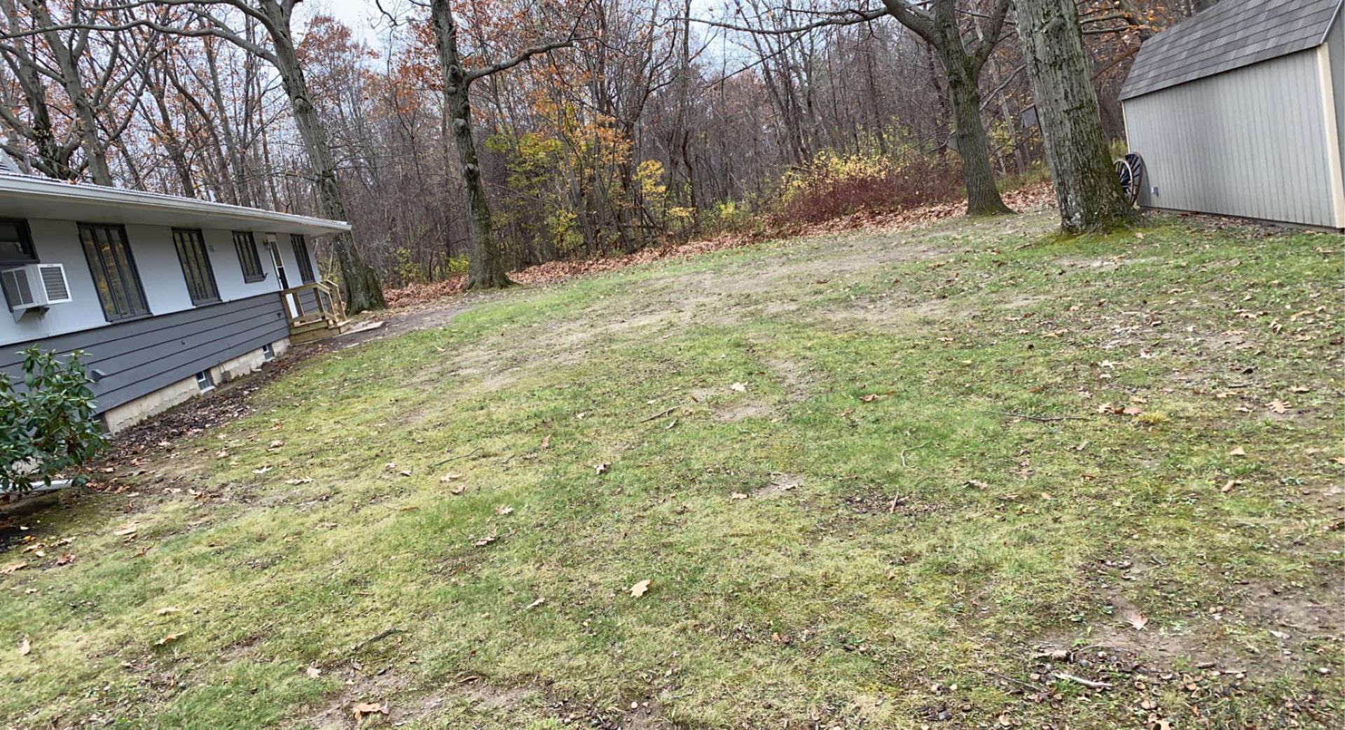 A house is sitting on top of a grassy hill next to a shed.