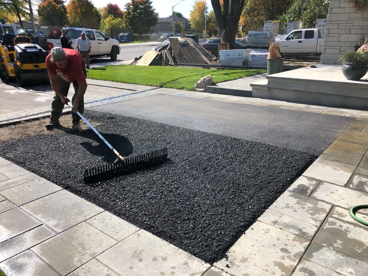 Un homme ratisse l'asphalte frais sur une allée, à côté d'une allée pavée, au soleil couchant.