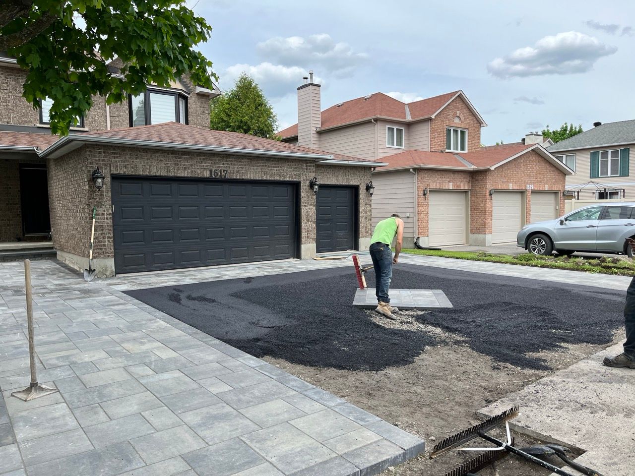 Une personne pavage une allée avec de l'asphalte noir frais devant une maison en briques.