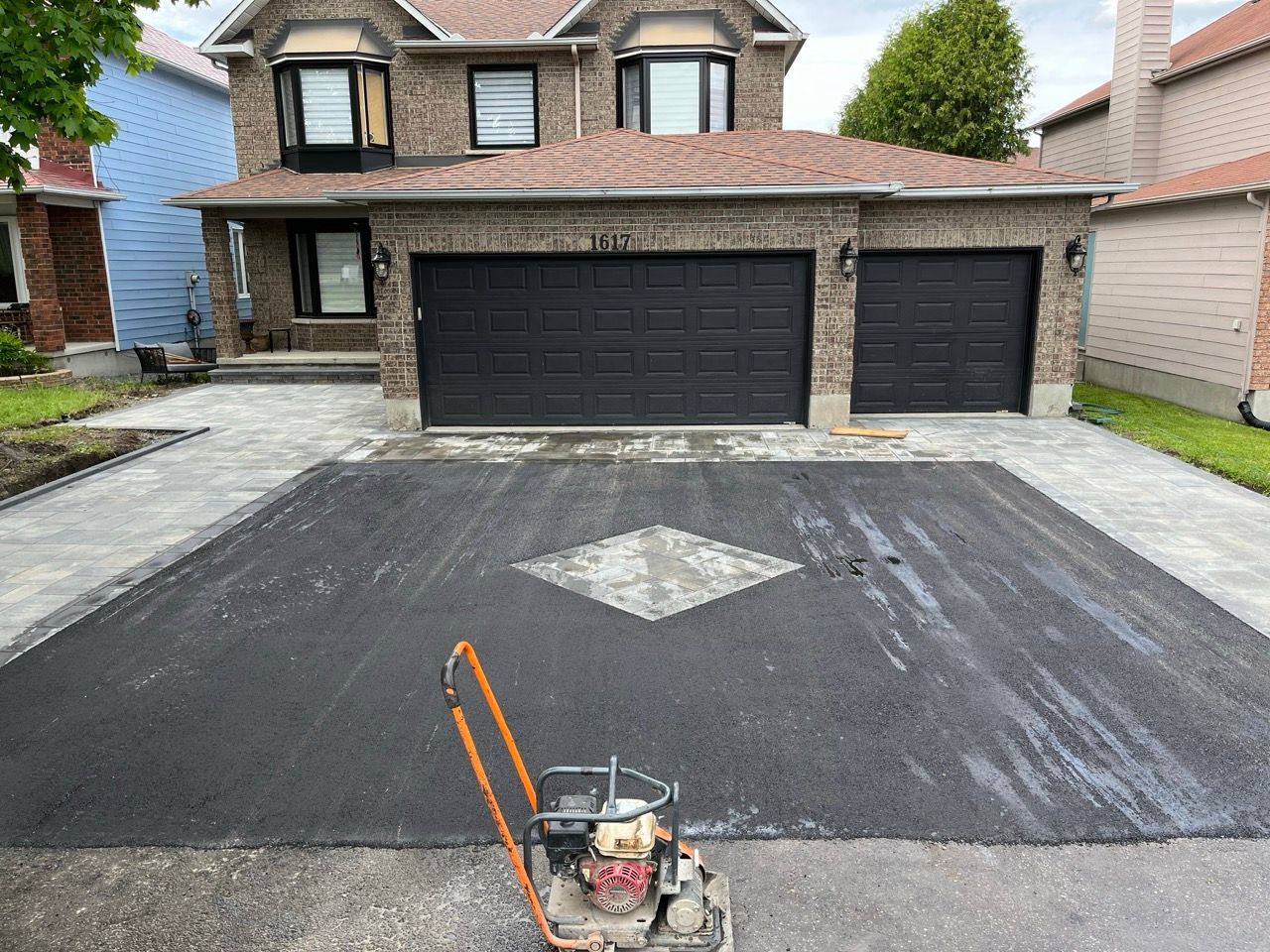 Allée asphaltée nouvellement pavée avec diamant décoratif au centre, garage pour deux voitures et maison en brique.