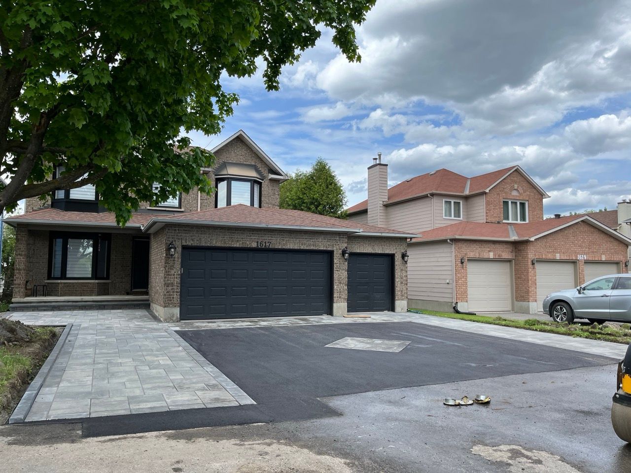 Maison en brique à deux étages avec nouvelle allée pavée et garage, à côté d'une maison similaire sous un ciel nuageux.