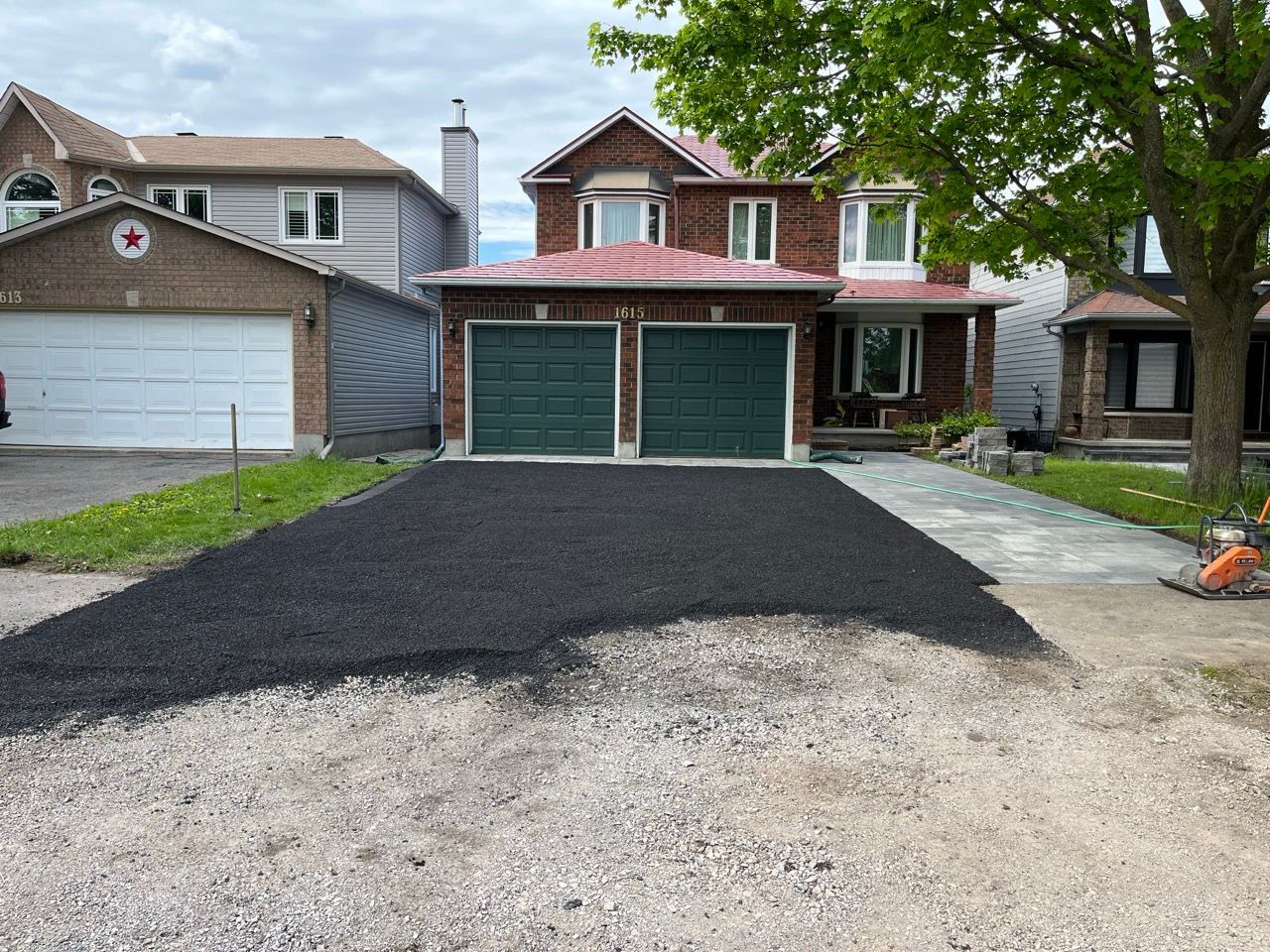 Une allée asphaltée nouvellement pavée devant une maison en briques à deux étages avec des portes de garage vertes.