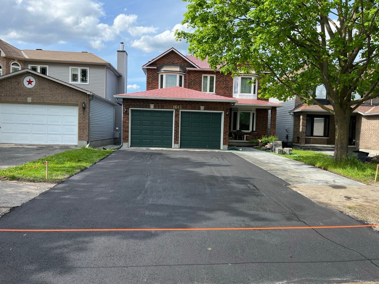Allée en asphalte noir nouvellement pavée devant une maison en briques à deux étages avec une porte de garage verte.