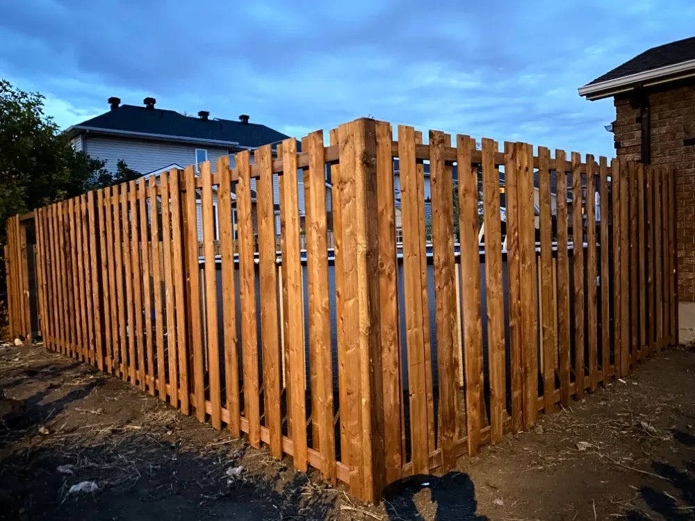 Clôture en bois autour d'un coin de propriété, teintée d'un brun chaud sous un ciel nuageux.