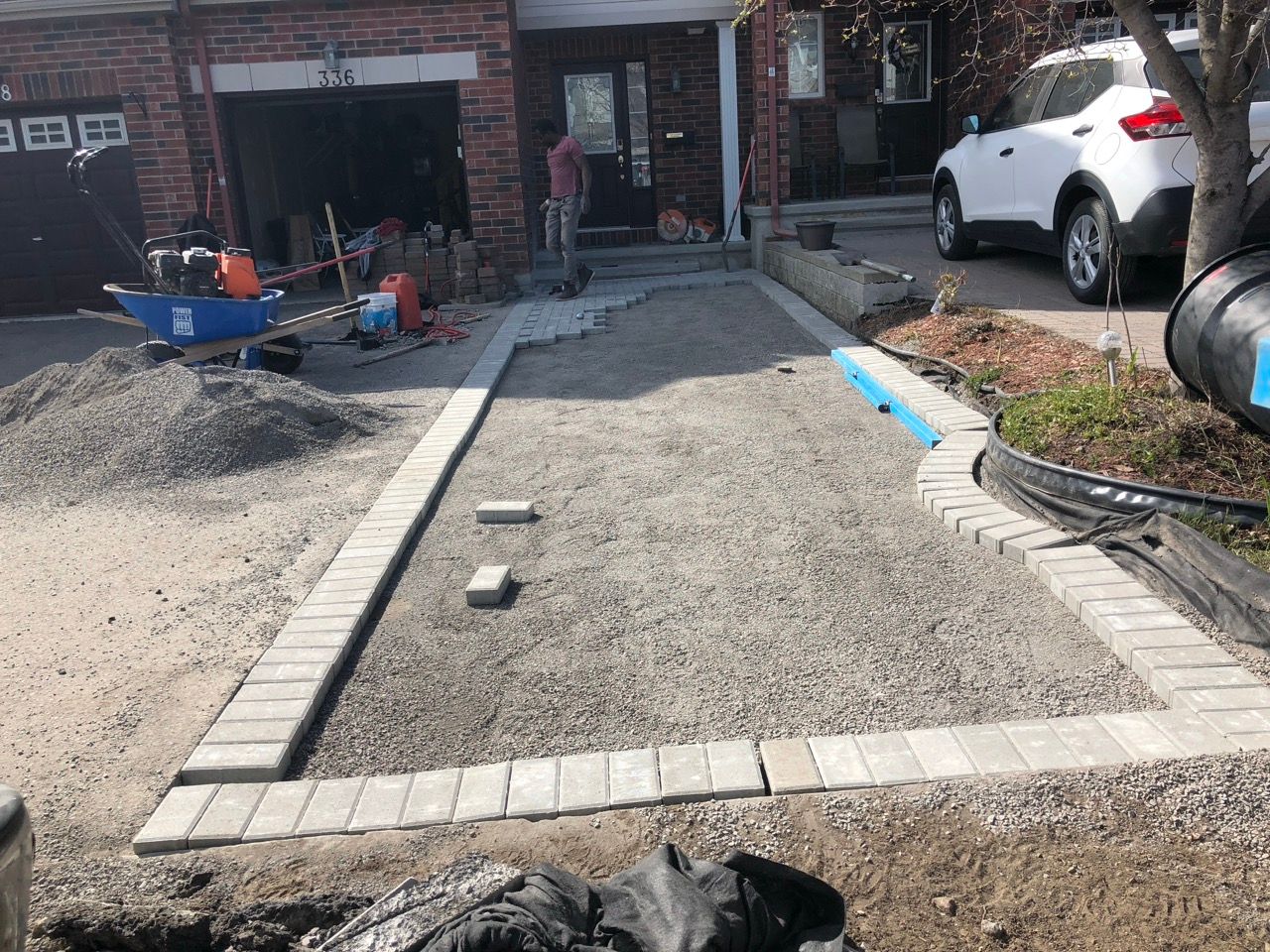 Construction d'une allée : bordure de gravier et de briques, ouvrier debout, maison en arrière-plan.