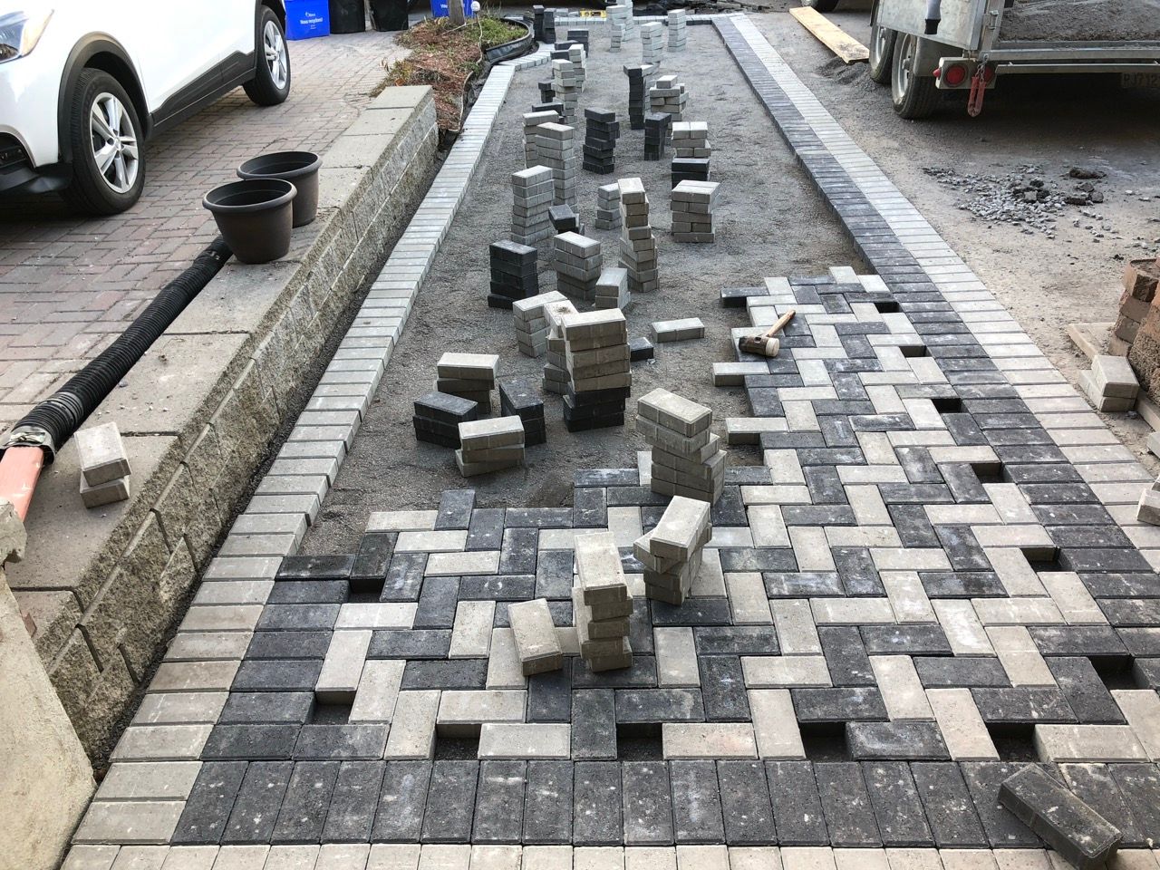 Pose de pavés : ouvriers posant des briques grises et noires en chevrons sur une allée.