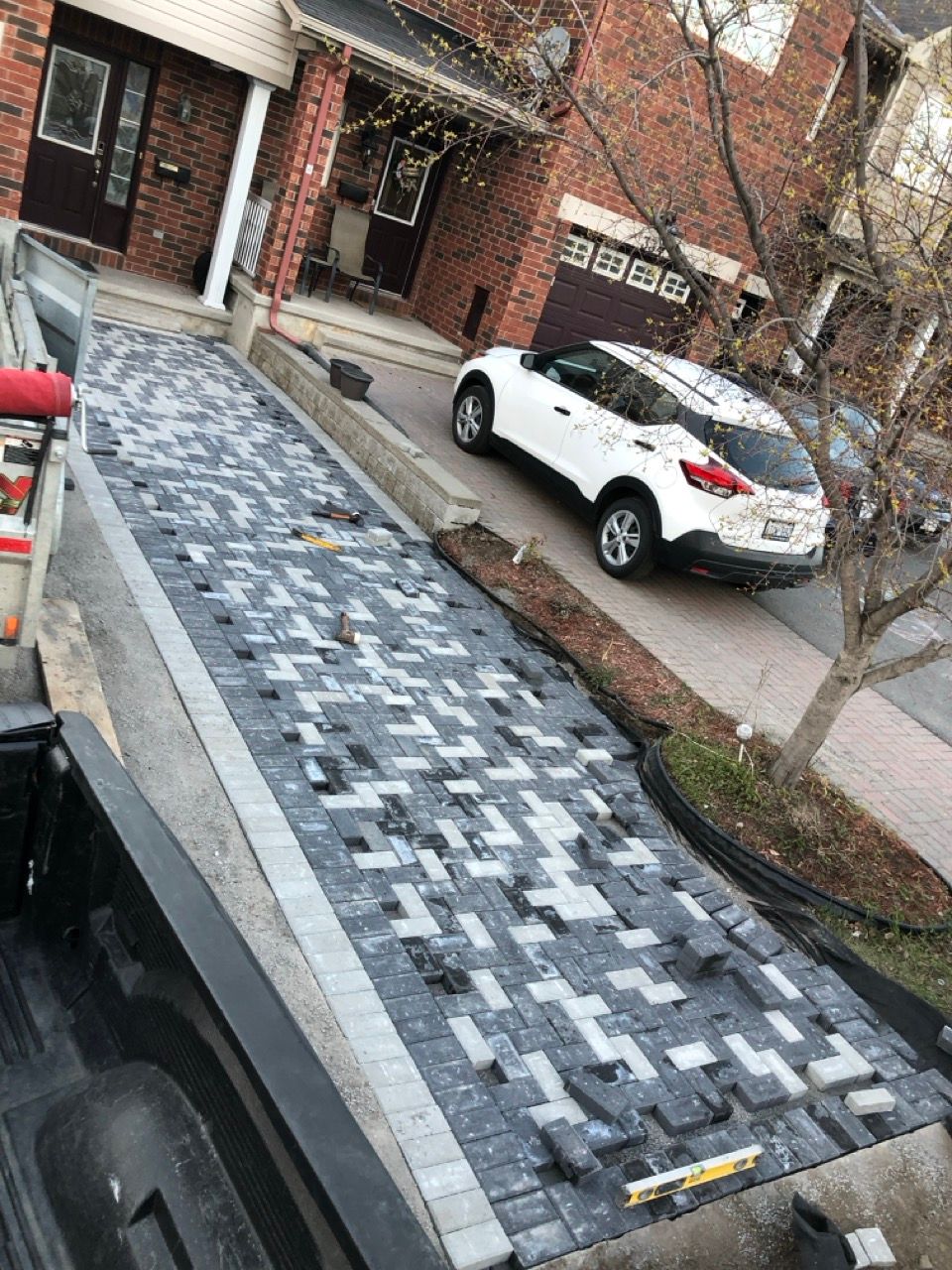 Allée pavée de briques grises et bleues à motifs. Un SUV blanc est garé à côté.