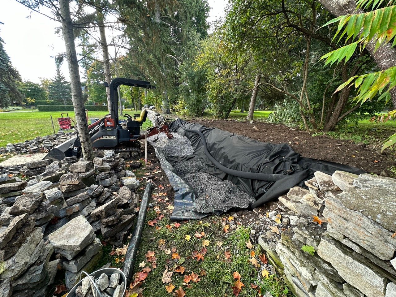 Une petite excavatrice travaille sur un projet d'aménagement paysager entre des murs de pierre.