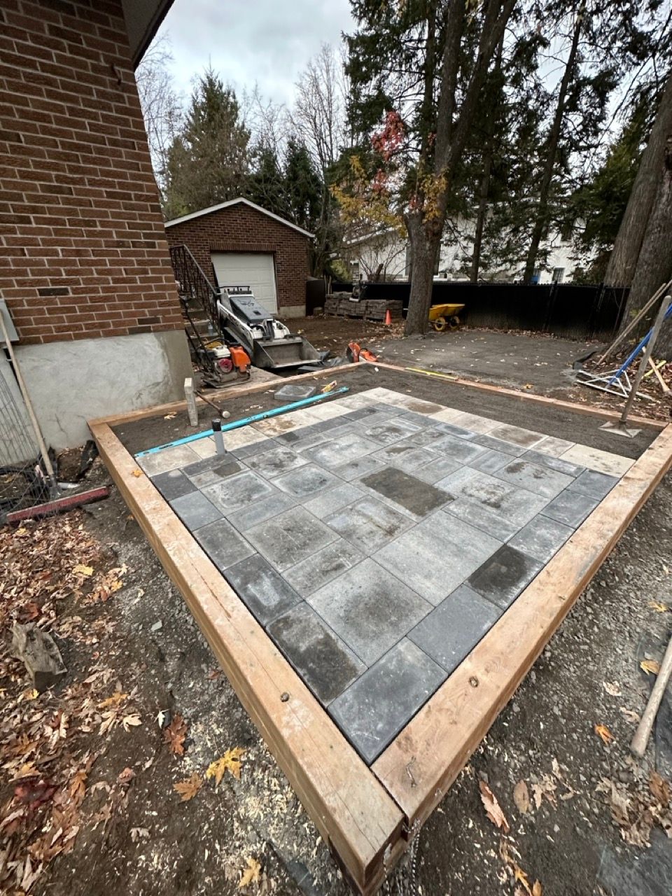 Un patio à ossature de bois avec des pavés gris et noirs en construction dans une cour arrière.