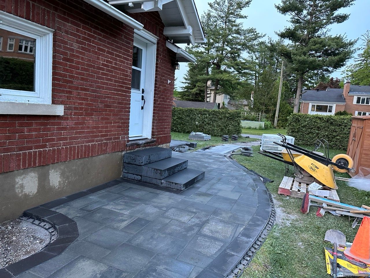 Bâtiment en briques avec escaliers et allée pavés. Outils de construction à proximité.