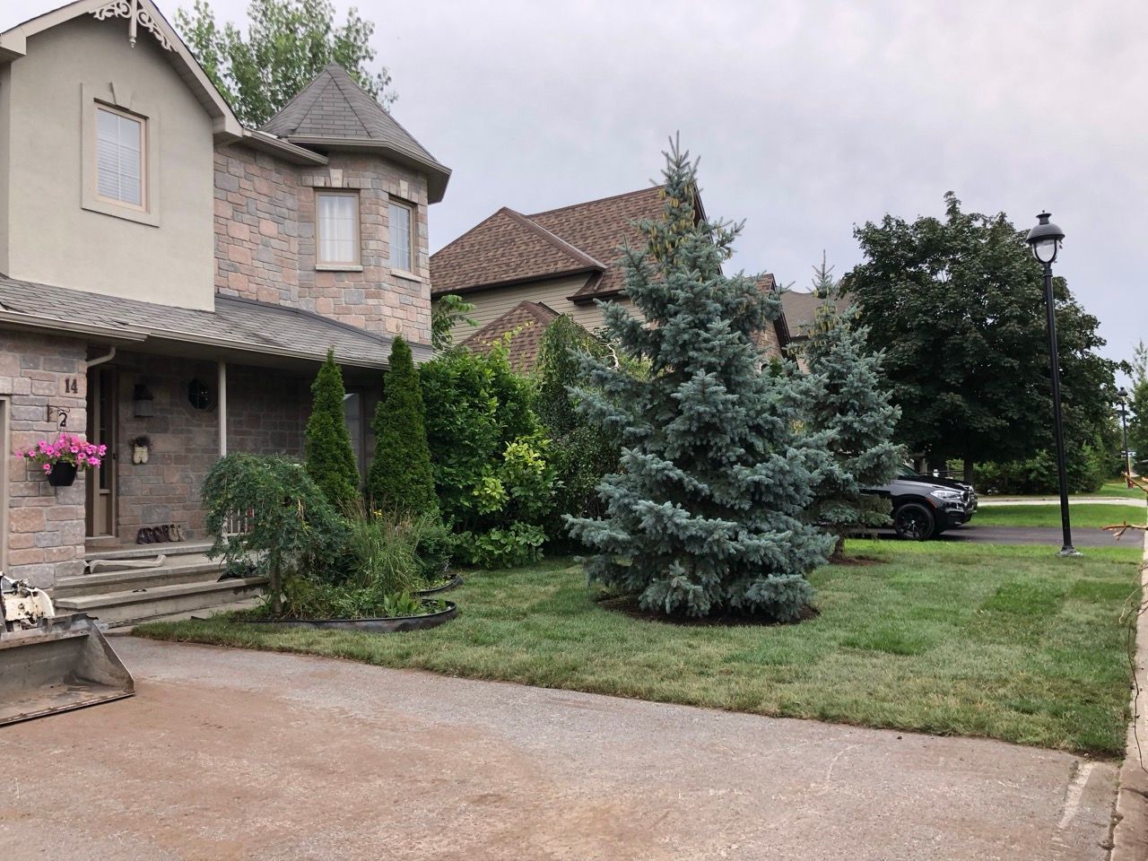 Maison en pierre avec pelouse soignée et arbres variés. Ciel nuageux.