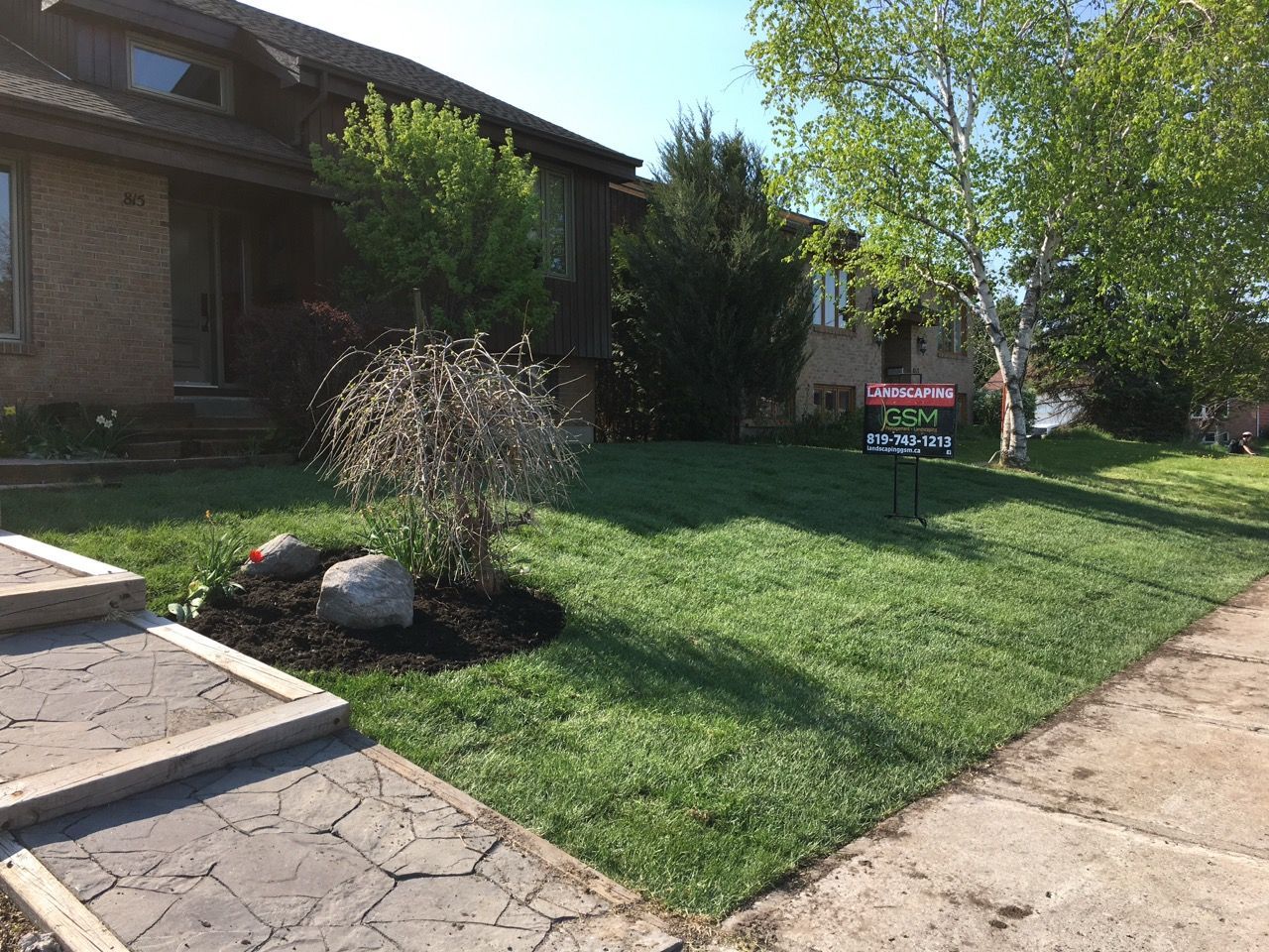 Une maison avec une pelouse verte, des arbres et un panneau « À vendre ». Des marches marron mènent à la porte d'entrée.