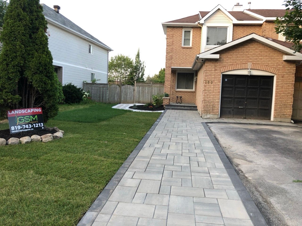 Allée en briques menant à une maison en briques avec garage. À gauche, une pelouse verdoyante.