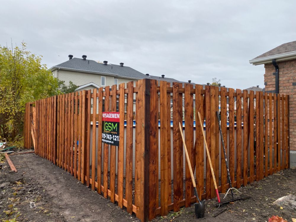 Clôture en bois dans l'arrière-cour, fraîchement teintée avec des outils appuyés contre elle par une journée nuageuse.
