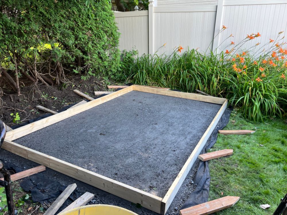 Cadre rectangulaire recouvert d'asphalte foncé, dans un jardin. Des planches de bois bordent le périmètre ; gazon et plantes l'entourent.