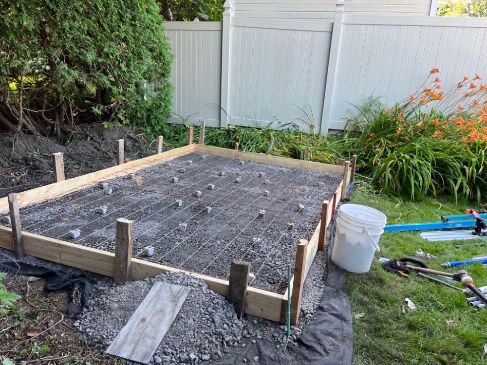 Chantier de construction avec ossature bois pour dalle béton, grille ferraillage et gravier, extérieur.