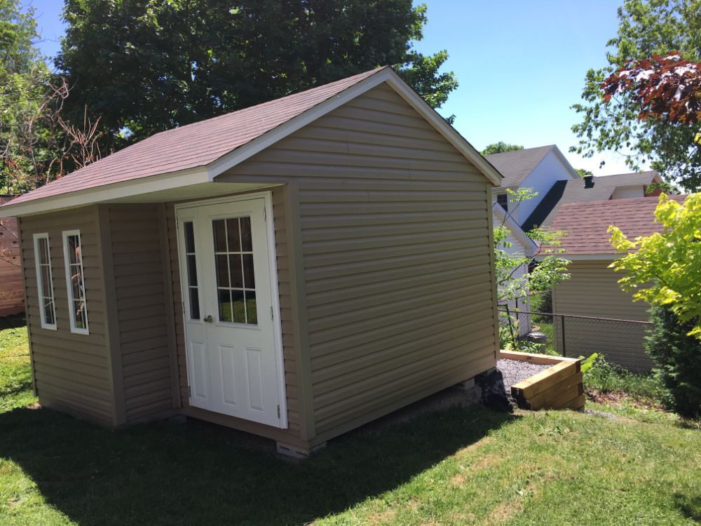 Hangar beige avec porte et fenêtres blanches, sur l'herbe verte sous le ciel bleu.